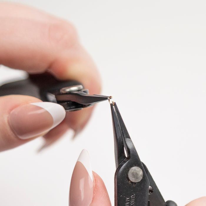 Close-up of a person using a pair of black micro precision pliers on a white background