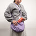 Person wearing a gray sweater and holding a purple bag with a small canister of argon gas.